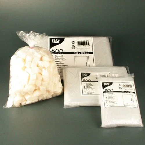 Ein durchsichtiger Plastikbeutel mit weißen Zuckerwürfeln liegt neben drei Stapeln Starpak 500 Flachbeuteln, transparentes LDPE, jeweils in Markenverpackung mit Produktinformationen und der Zahl 500, was diese hochwertige Verpackungslösung hervorhebt.